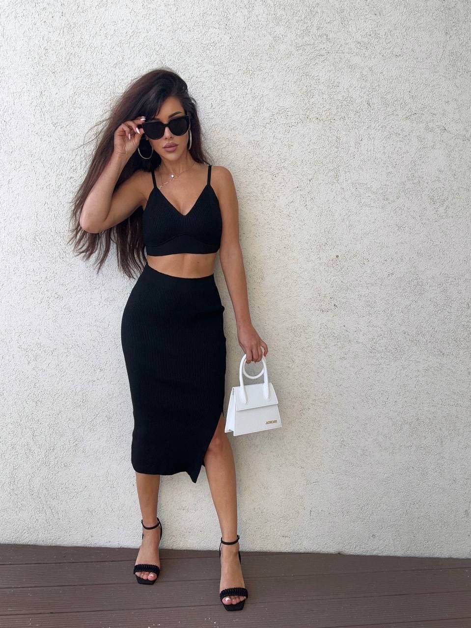 Woman in black outfit holding a white handbag against a light background