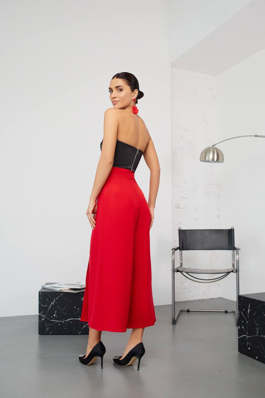 Woman wearing a black top and red jumpsuit in a modern interior setting