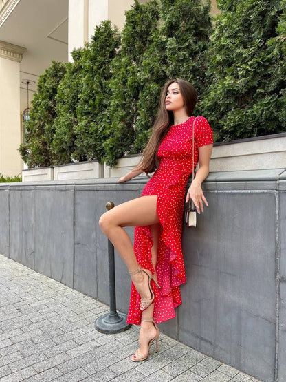 Woman in a red dress leaning against a wall with greenery in the background