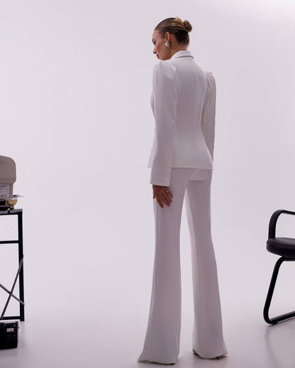 Person wearing a white suit standing in a minimalistic room with a chair and table.