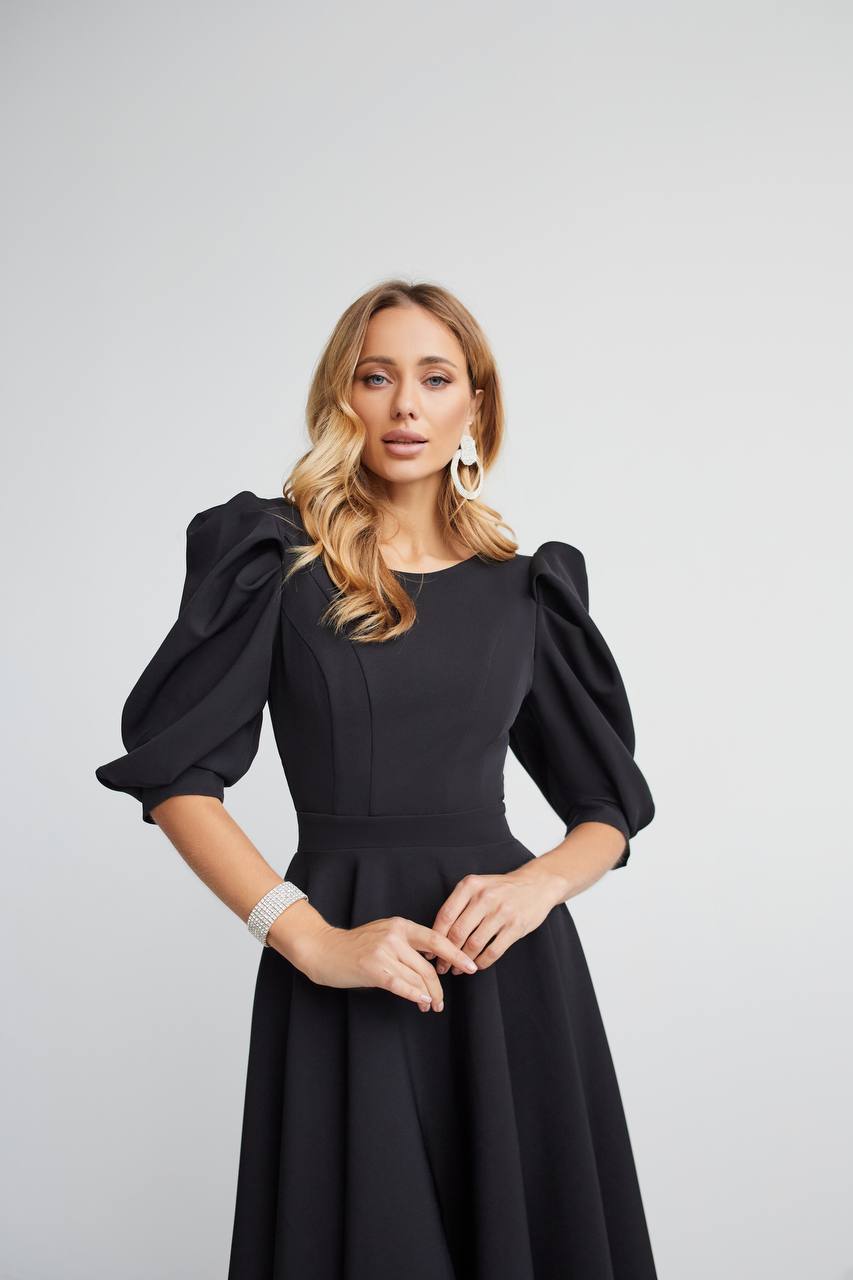 Woman wearing a black dress with puffed sleeves against a light gray background