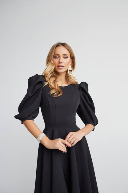 Woman wearing a black dress with puffed sleeves against a light gray background