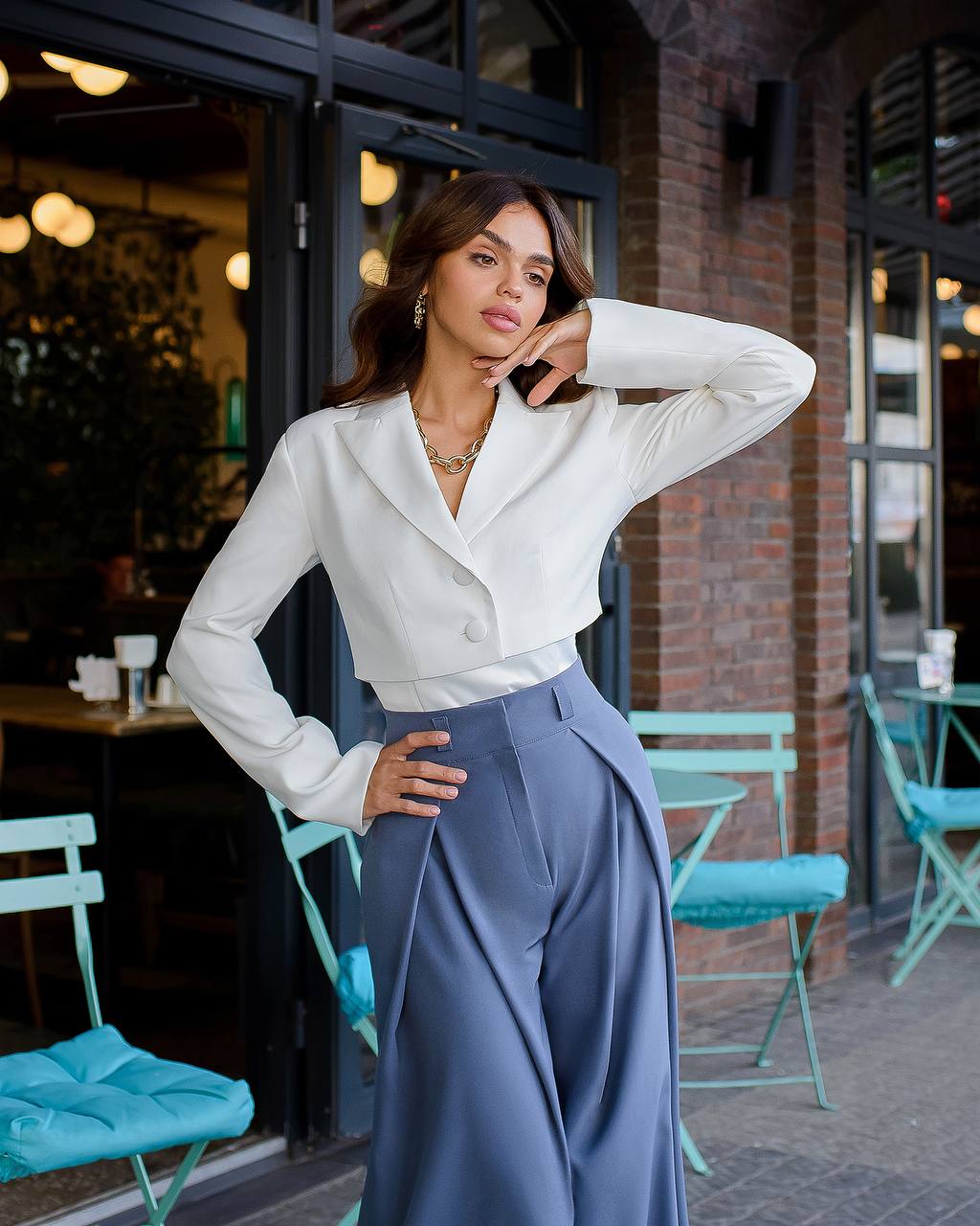 Woman in a white blouse and blue pants standing in an outdoor cafe setting.