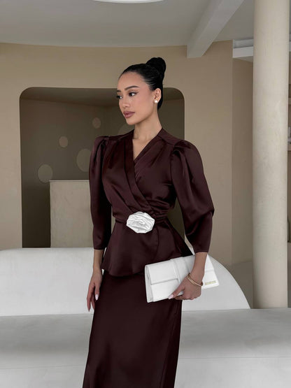 Woman in a dark brown outfit holding a white clutch in an indoor setting