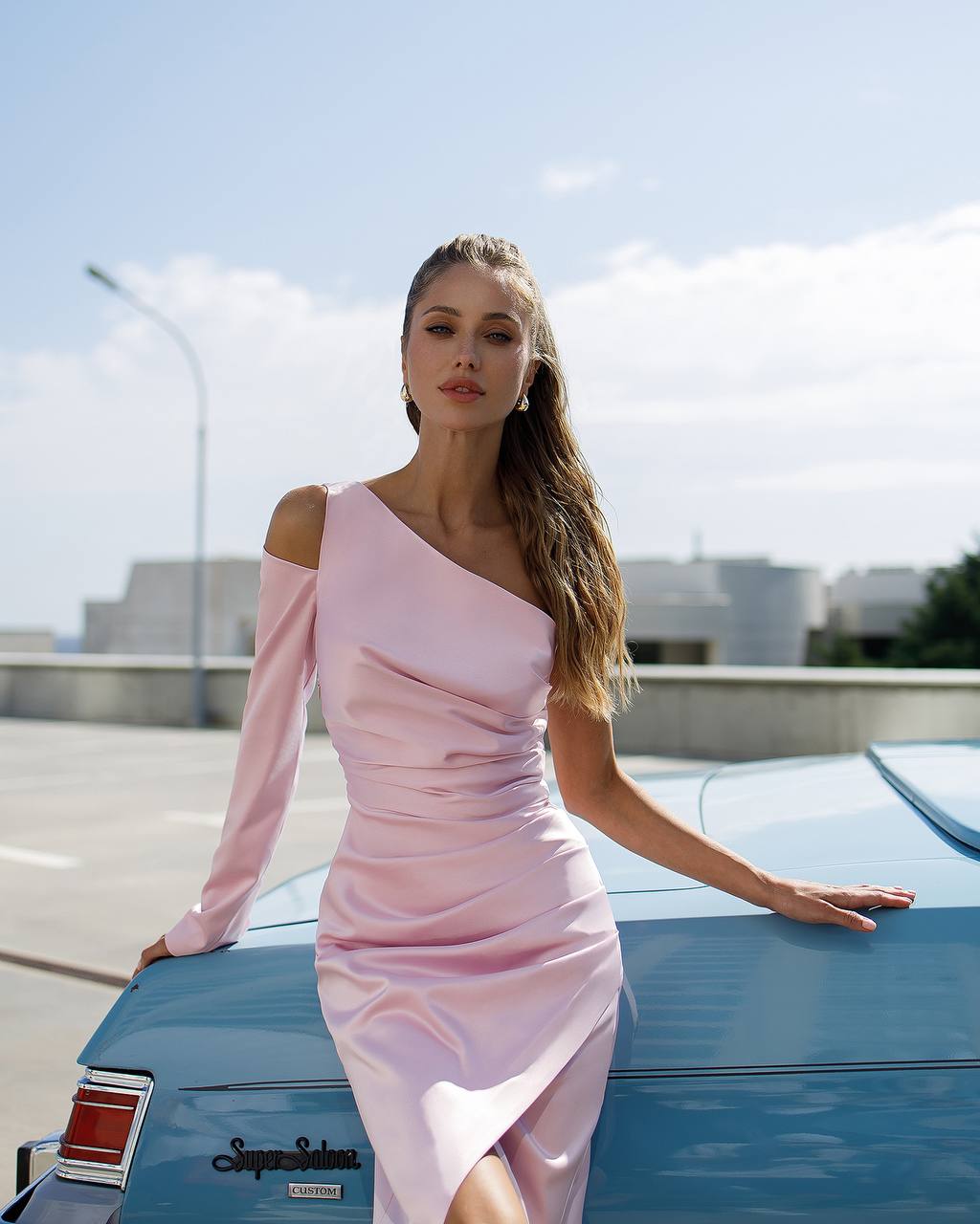 Woman in a pink dress leaning on a blue car with a clear sky background
