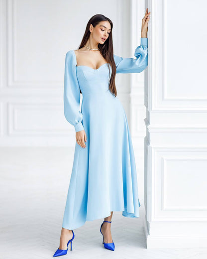 Woman wearing a light blue dress with long sleeves in a minimalistic setting