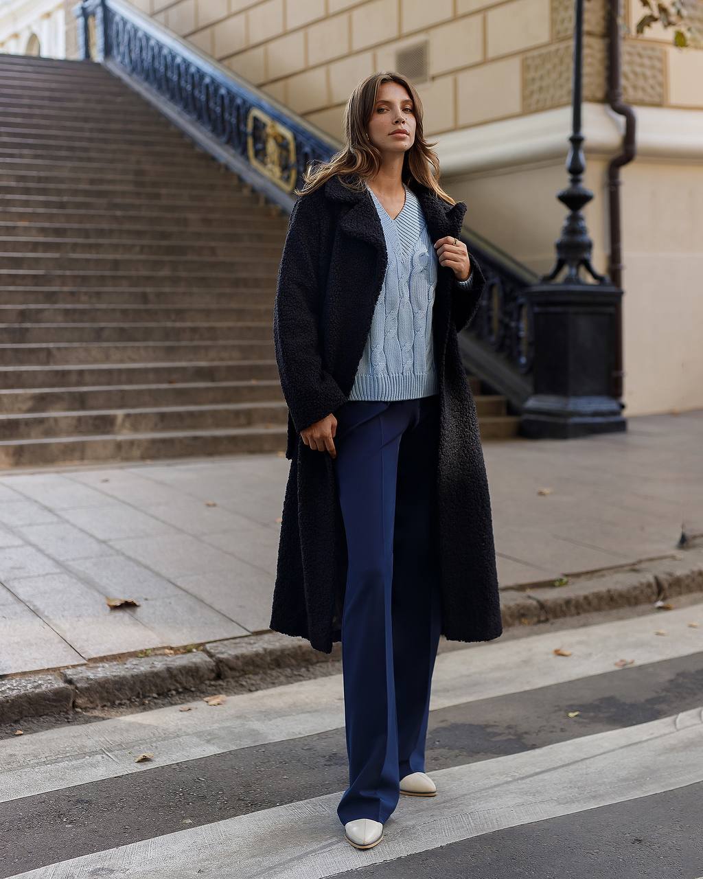 Woman in a black coat and blue pants walking on a city street.