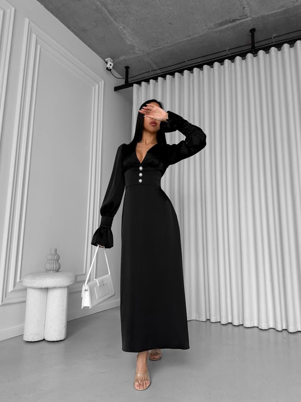 Woman wearing a black dress in an indoor setting with white walls and a curtain.
