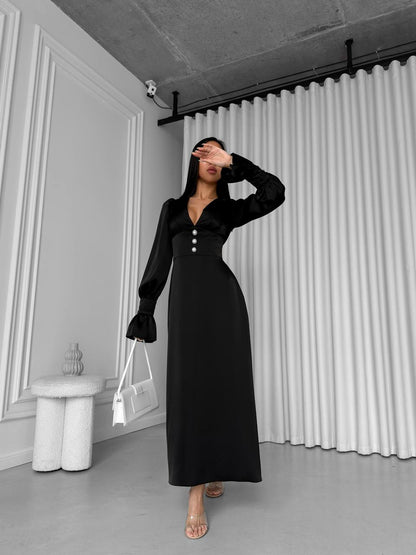 Woman wearing a black dress in an indoor setting with white walls and a curtain.