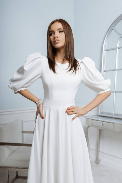 Woman wearing a white dress with puffed sleeves in a bright room.