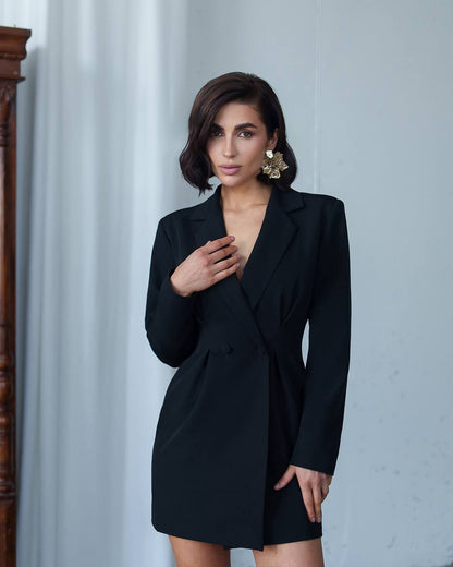 Woman wearing a black blazer dress against a light gray wall.