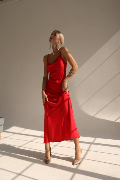 Woman in a red dress standing in a sunlit room with shadows on the wall.