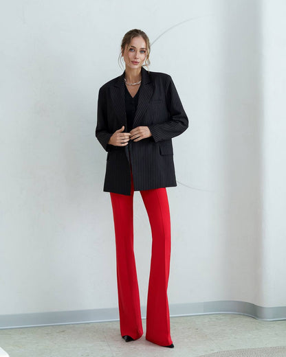 Woman wearing a black pinstripe blazer and red pants against a plain background