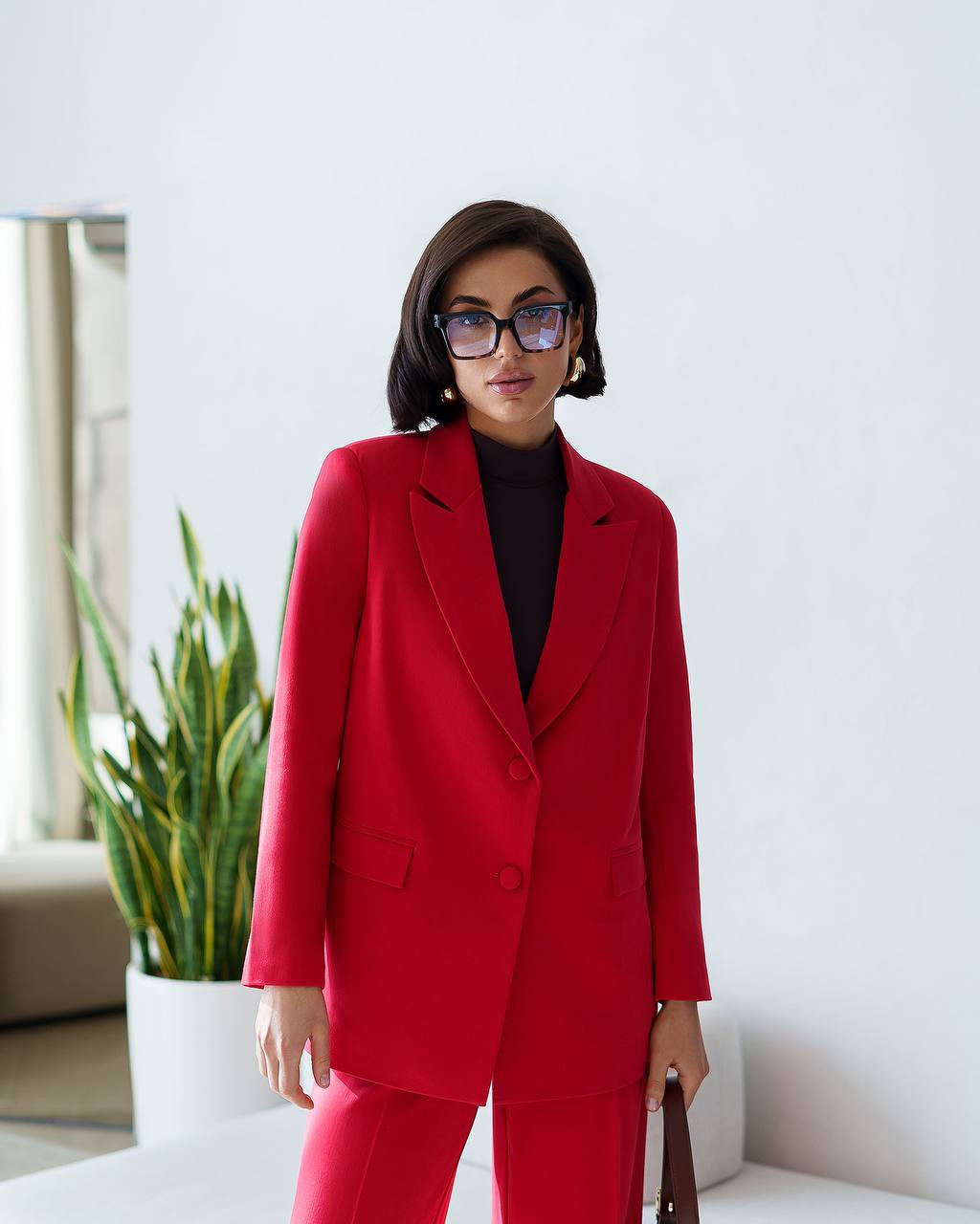 Woman wearing a red suit standing in a modern indoor setting with a plant in the background.