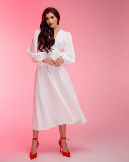 Woman wearing a white dress with long sleeves against a pink background