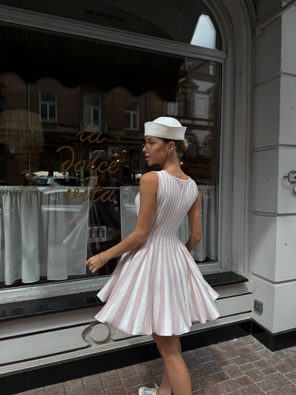 Woman in a white dress with red stripes walking past a store window.