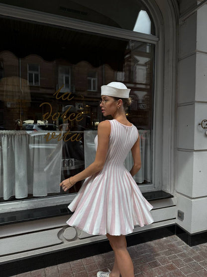 Woman in a white dress with red stripes walking past a store window.