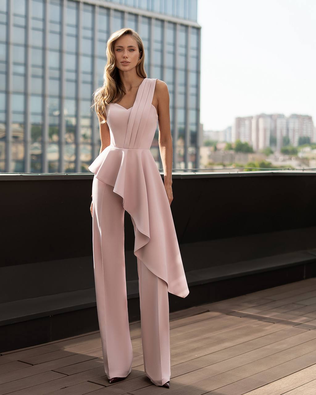 Woman in a light pink jumpsuit standing on a rooftop with cityscape background