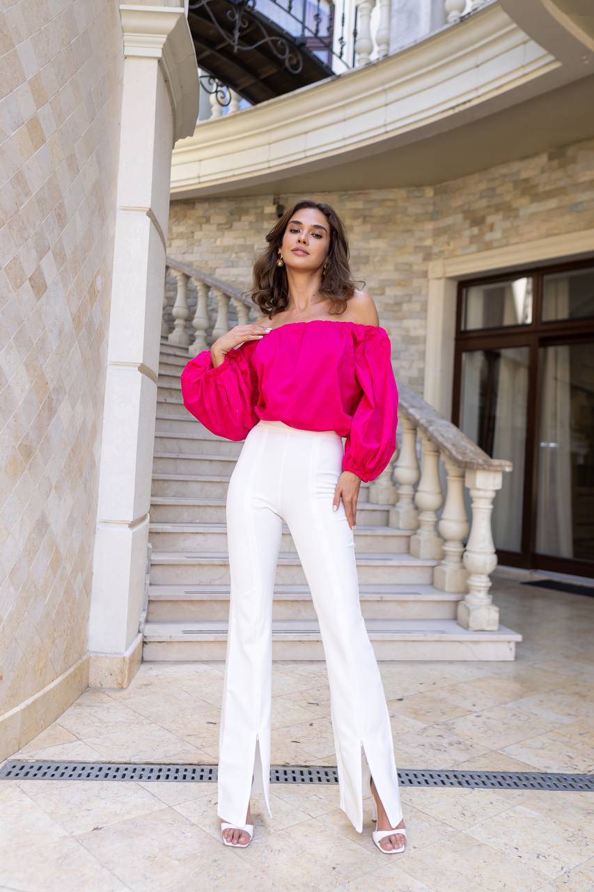 Woman in a bright pink top and white pants standing on a staircase.