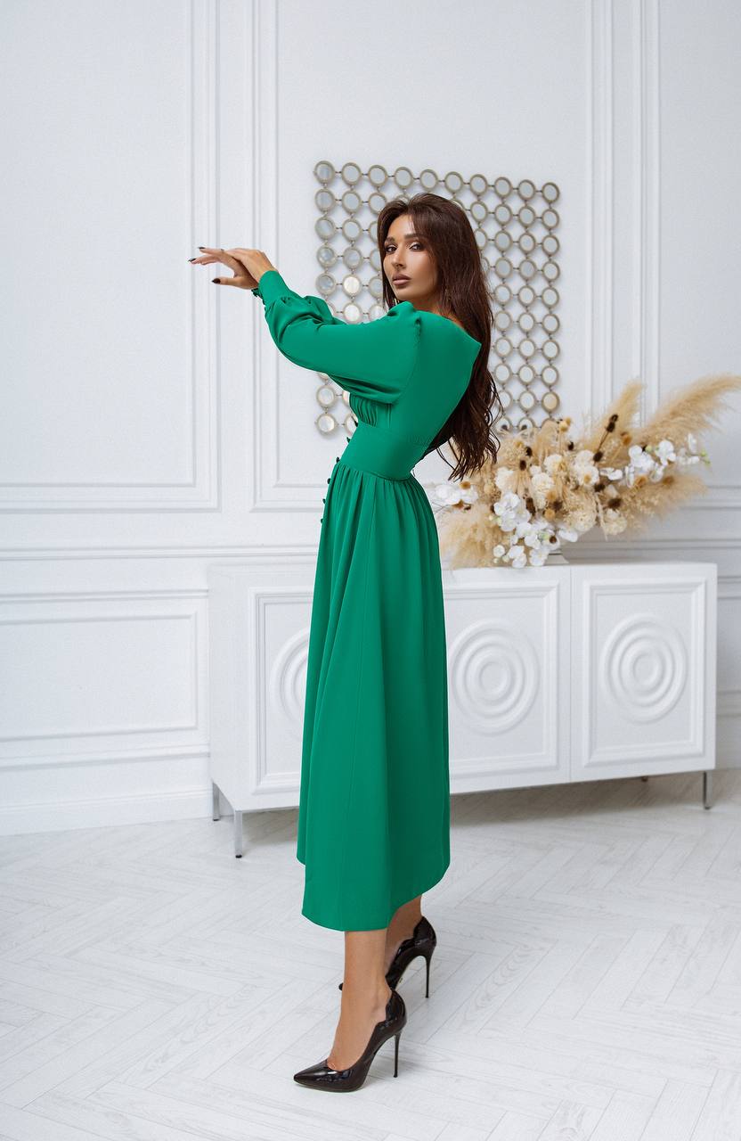Woman in a green dress standing in a stylish room with white walls and decorative elements.