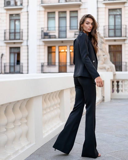 Woman in a black suit standing on a balcony with classical architecture in the background