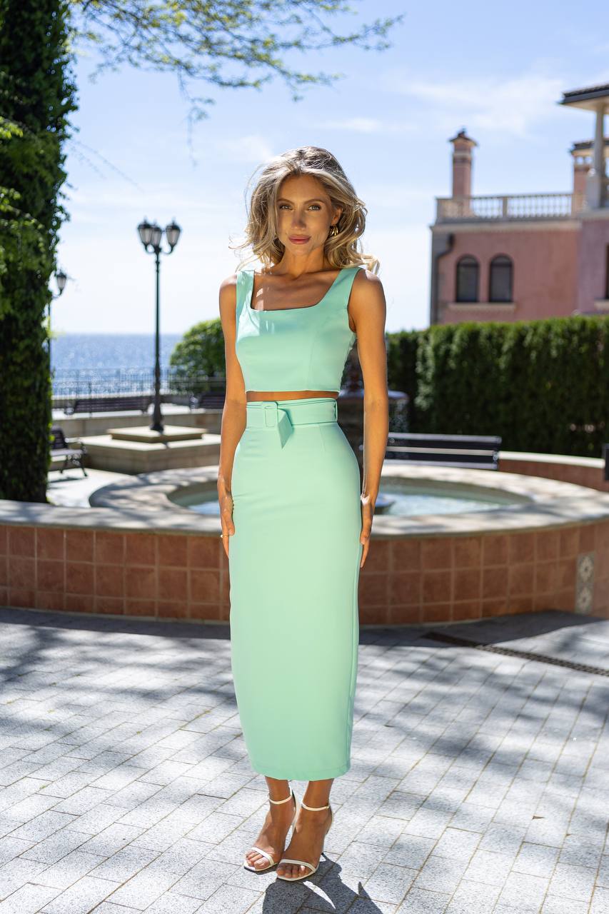 Woman in a light green dress standing outdoors with a scenic background