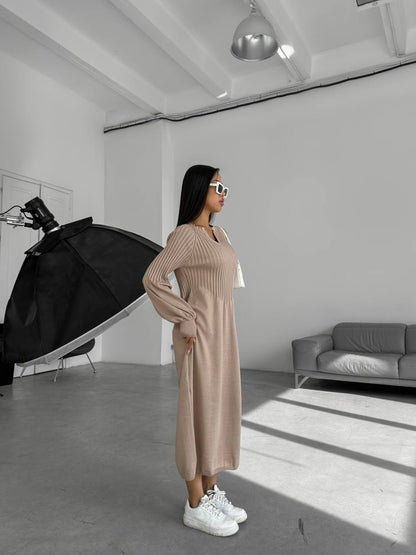 Woman in a beige dress standing in a studio with a black umbrella light and gray sofa.