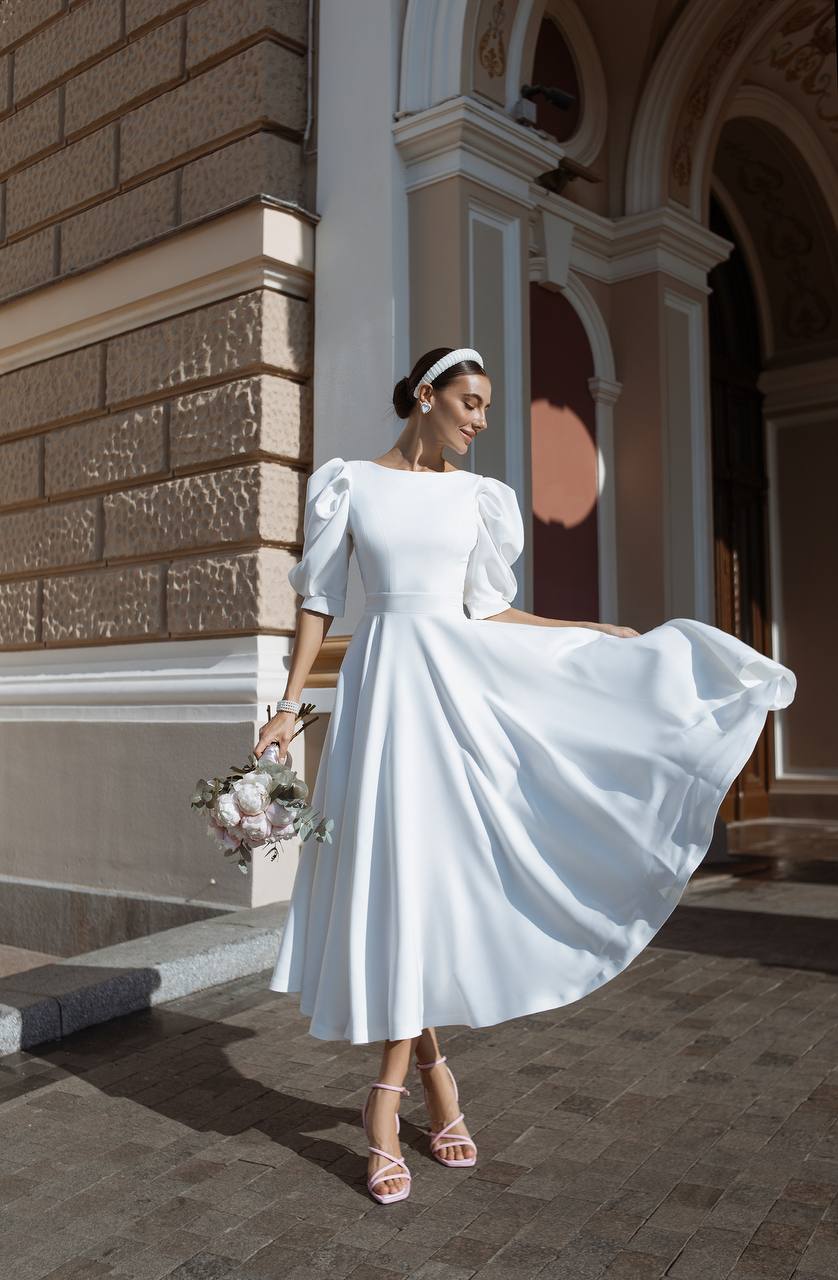 Woman in a white wedding dress standing in front of an architectural building.