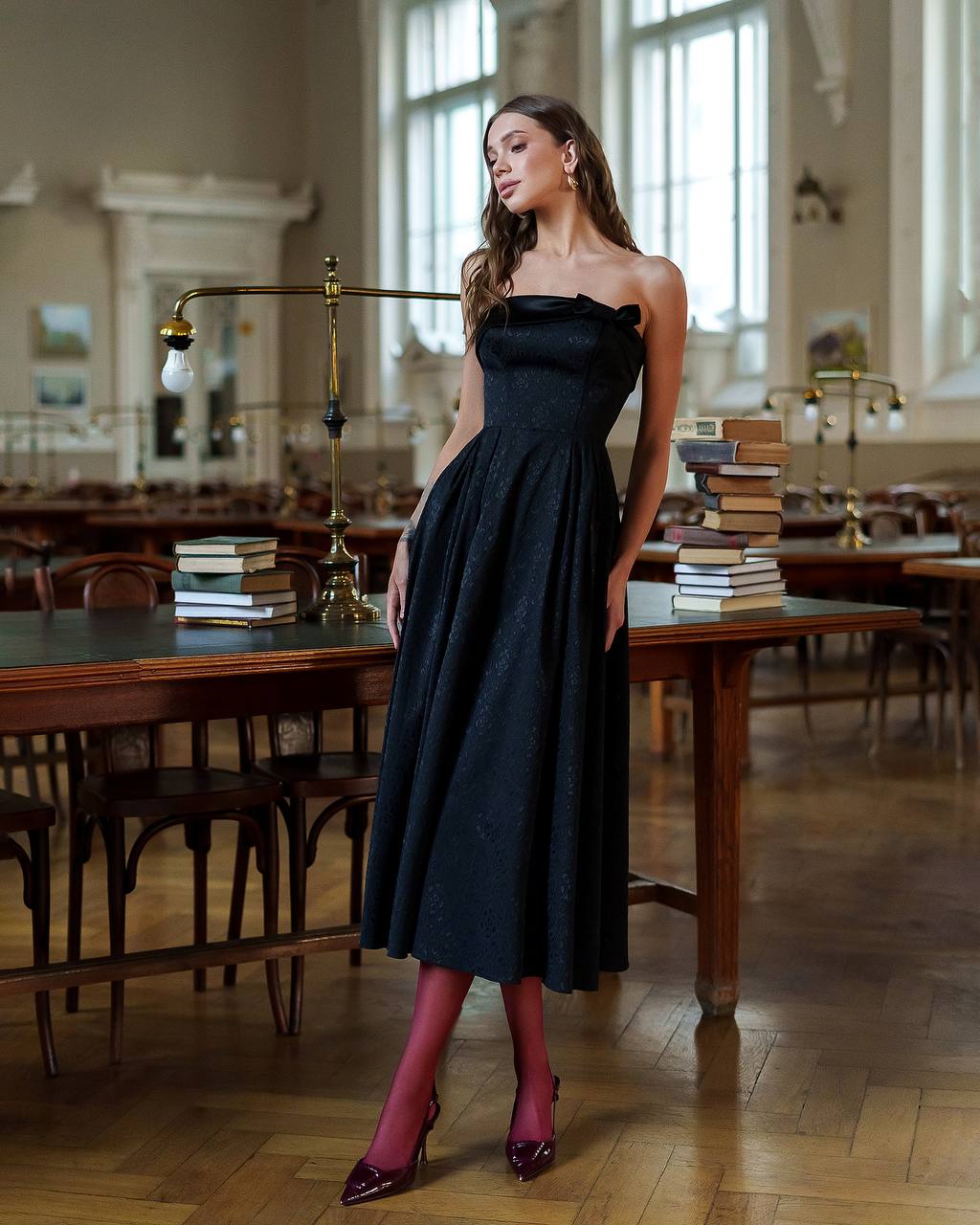 Woman in a black dress standing in a room with wooden tables and books.