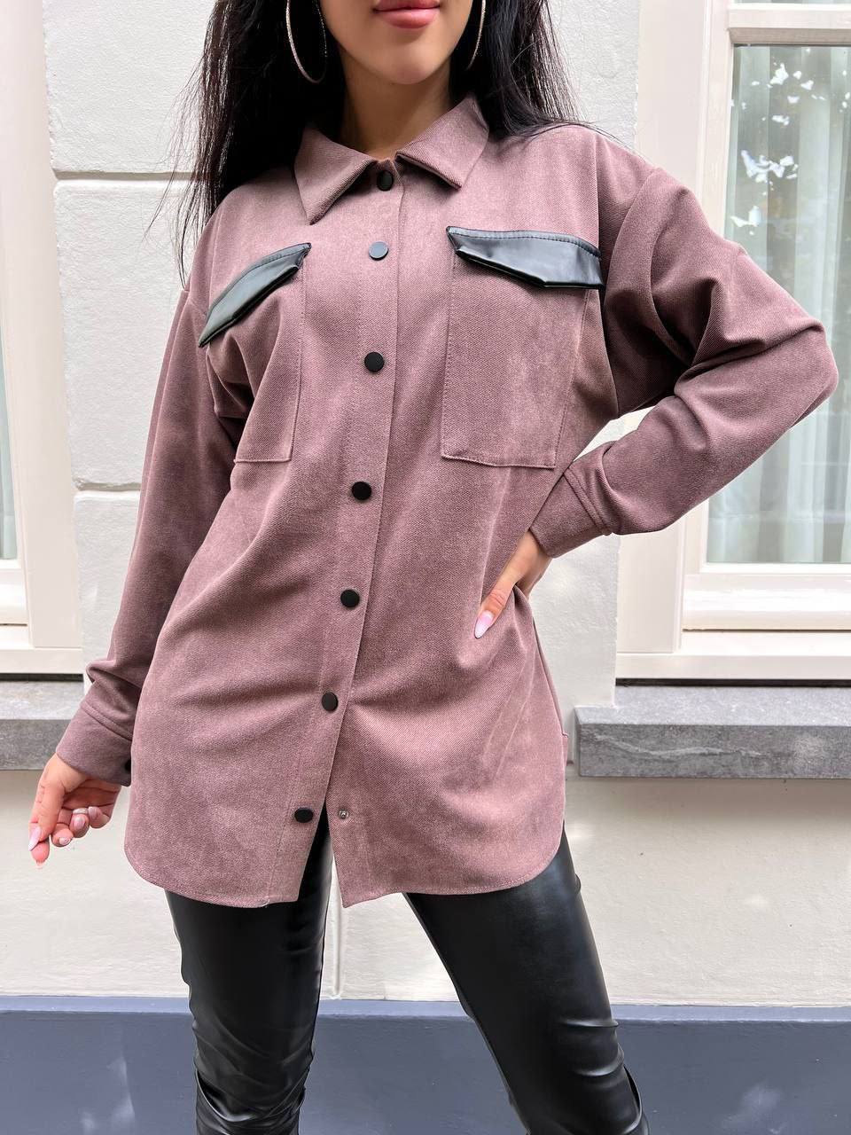 Person wearing a pink shirt with black leather accents in front of a window.