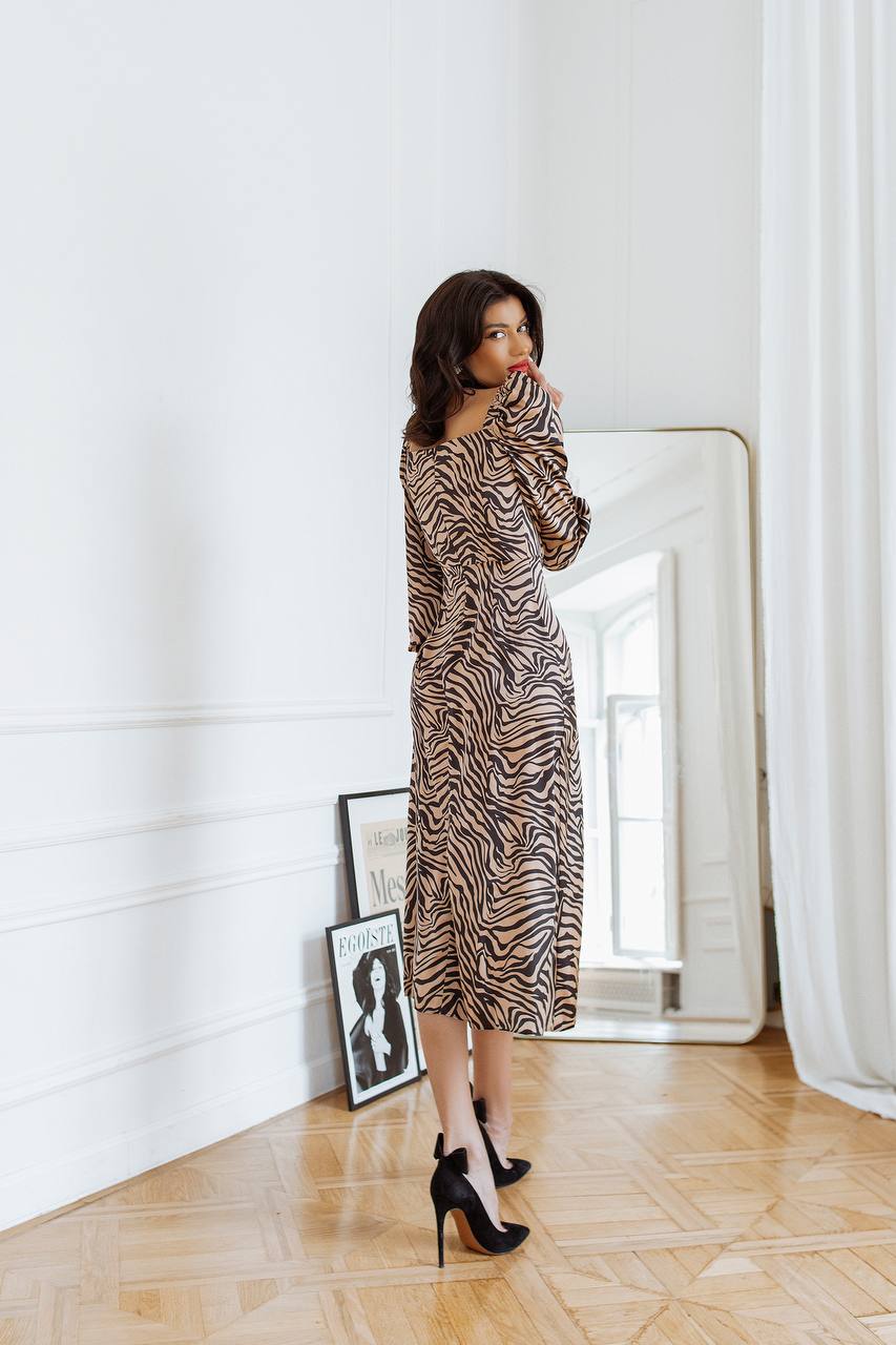 Woman in a zebra print dress standing in a room with a mirror and framed picture on the wall.