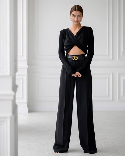 Woman wearing a black outfit with a Gucci belt against a white paneled wall.