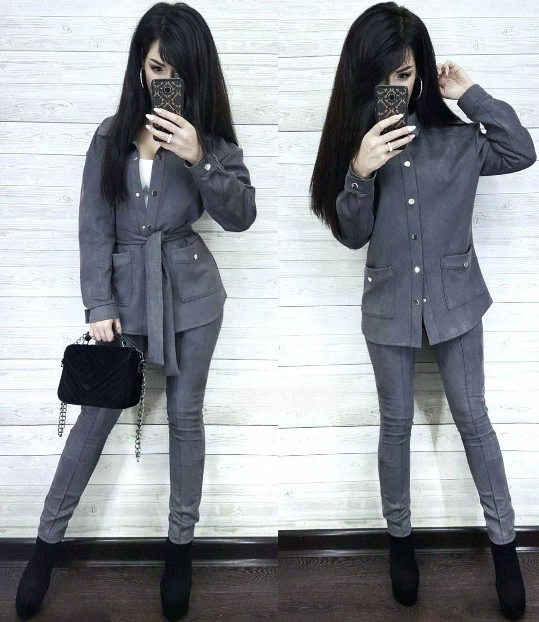 Woman in a gray suit taking a mirror selfie against a white wooden panel background