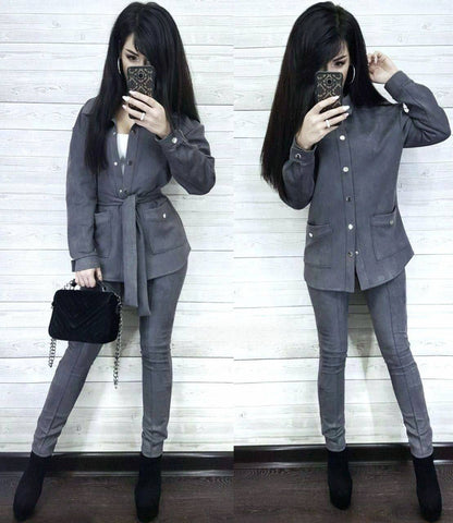 Woman in a gray suit taking a mirror selfie against a white wooden panel background