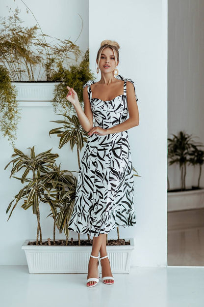 Woman in a black and white dress standing in front of potted plants.