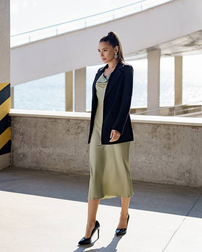 Woman in a black blazer and green dress standing under a bridge.