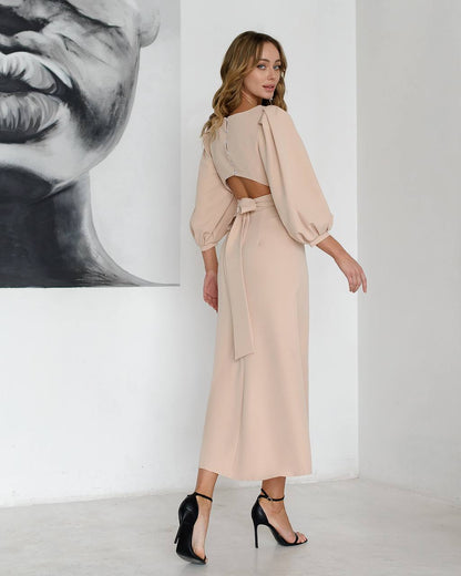 Woman wearing a beige dress with cut-out design in a minimalistic setting.
