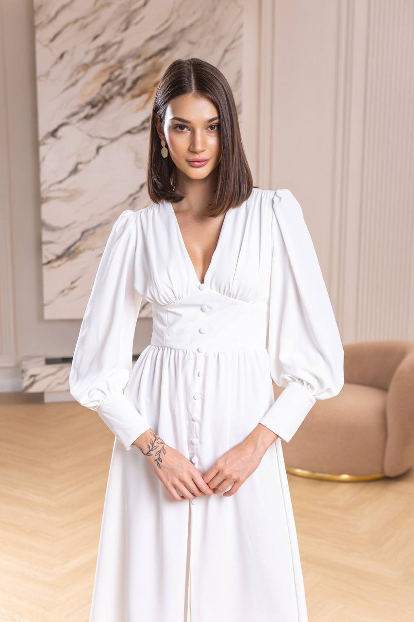 Woman wearing a white dress in an indoor setting with a marble wall and beige sofa.