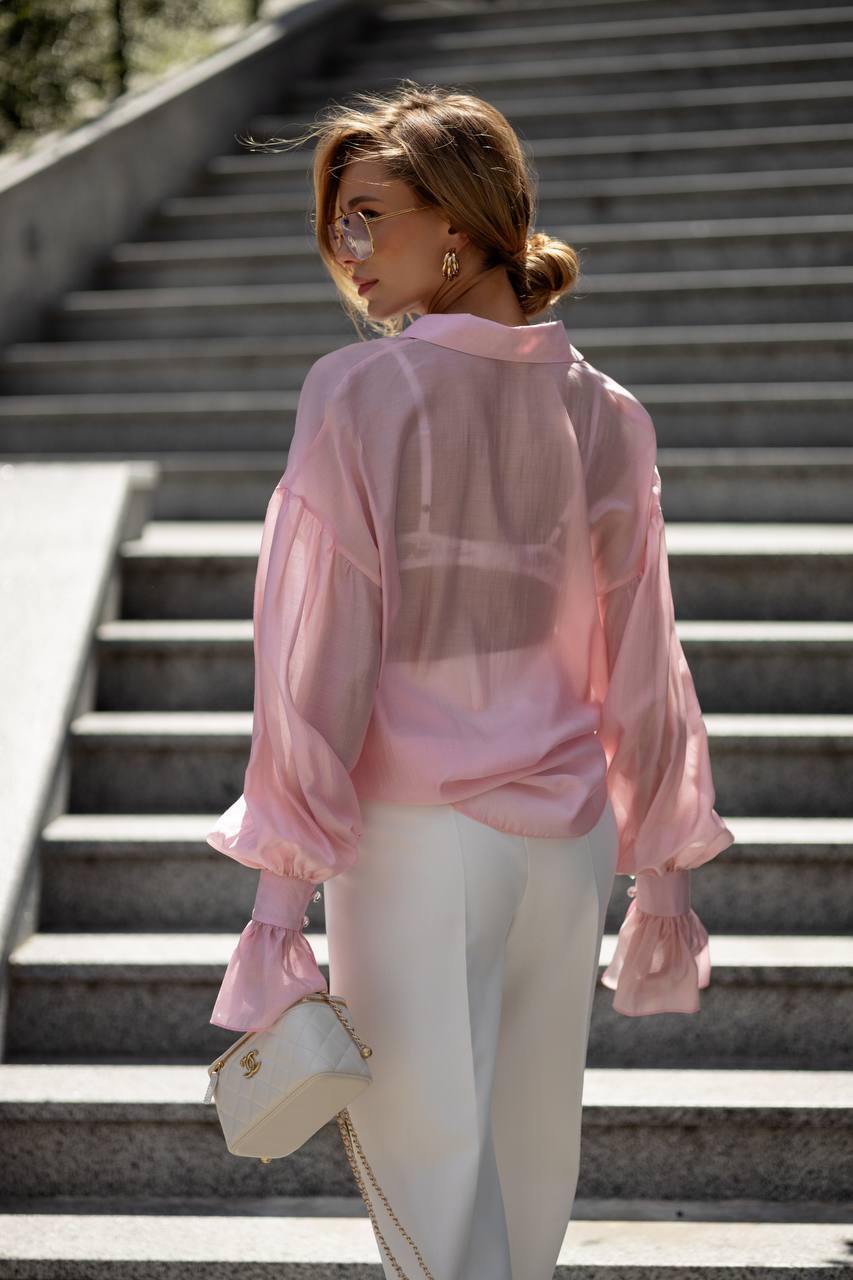 Woman in a pink sheer blouse and white pants standing on steps