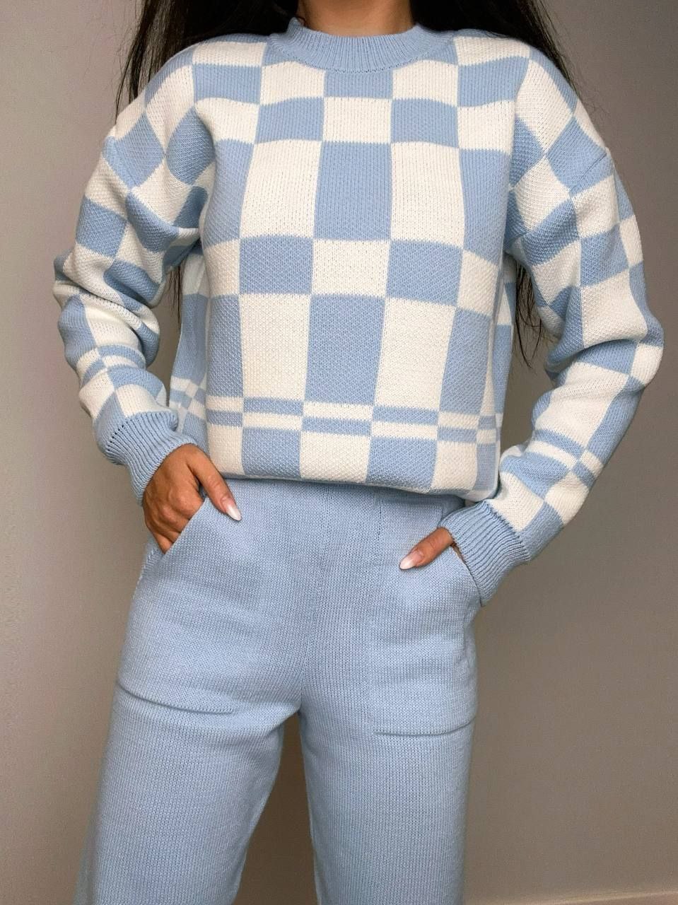 Person wearing a blue and white checkered sweater and pants against a neutral background