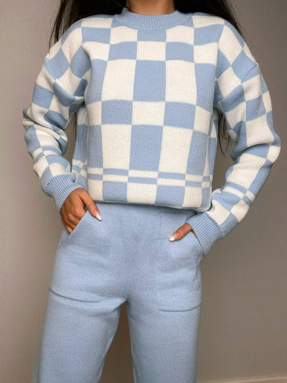 Person wearing a blue and white checkered sweater and pants against a neutral background