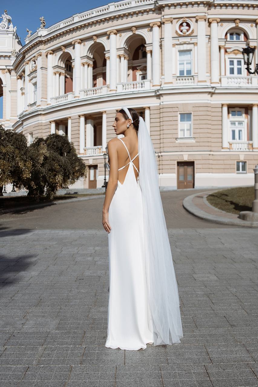Woman in a white wedding dress with a long veil standing in front of a classical building.