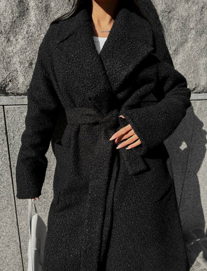 Person wearing a black coat against a stone wall.