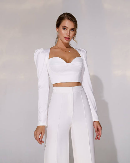 Woman wearing a white outfit with long sleeves and high-waisted pants against a plain background