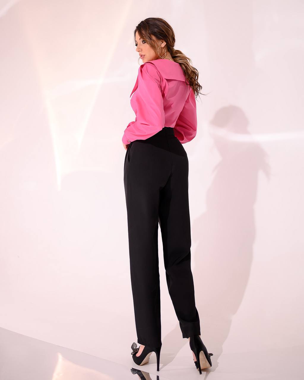 Woman wearing a pink blouse and black pants against a white background