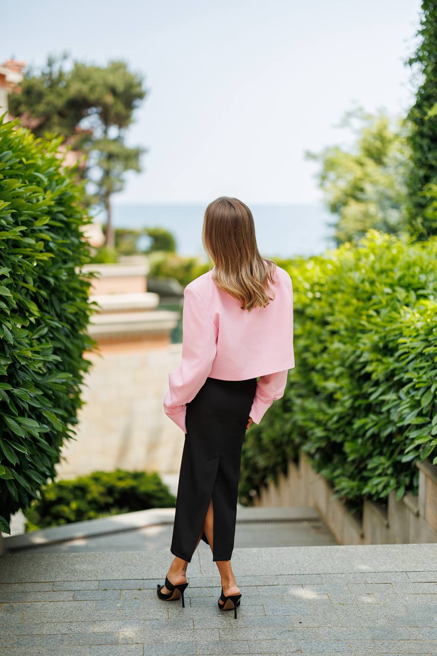 Woman in a pink coat walking away from the camera on a path with greenery.