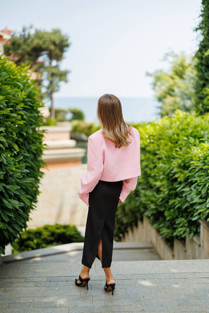 Woman in a pink coat walking away from the camera on a path with greenery.