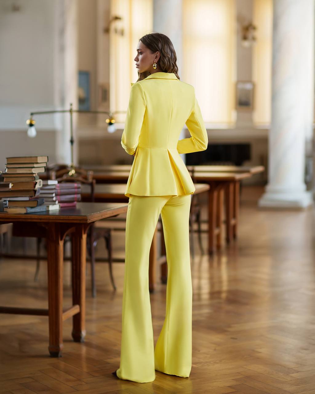 Person wearing a bright yellow suit standing in a room with wooden tables and columns.