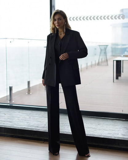 Woman in a black suit standing in a modern indoor setting with large windows.