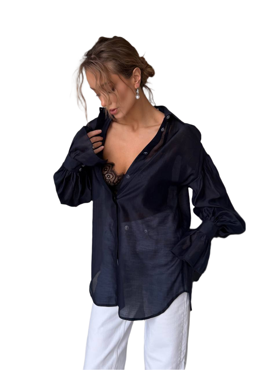 Woman wearing a black sheer blouse over a black top with white pants on a white background
